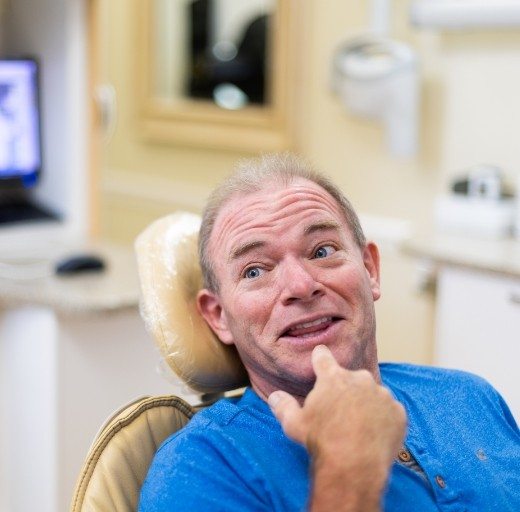 Man pointing to smile discussing candidacy for dental implant tooth replacement
